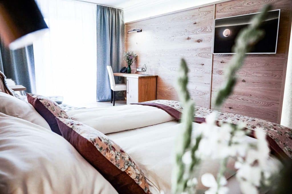Hotel Gut Edermann Zimmerausschnitt, Fenster, Bett, Schreibtisch, Wand mit Holzvertäfelung und TV