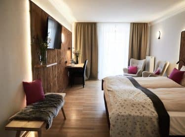 Hotel Gut Edermann Zimmer mit Fenster, Sessel, Bett, Schreibtisch. Sitzbank, Wand mit Holzvertäfelung